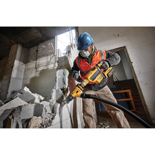 Worker uses DEWALT demolition hammer to break concrete wall in construction site.