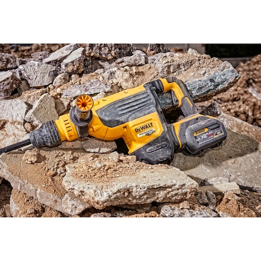 A DEWALT cordless rotary hammer drill lying on broken concrete and rubble at a construction site.
