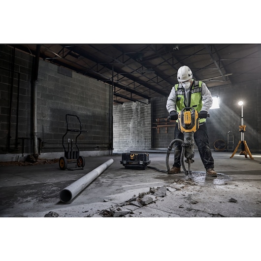 Worker uses DEWALT DCH966Z2, DCH966Z2-XE drill on concrete floor in industrial site. Photography product category.