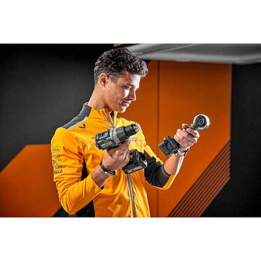 Person in yellow jacket holding two DEWALT power tools in a modern, orange-accented room.