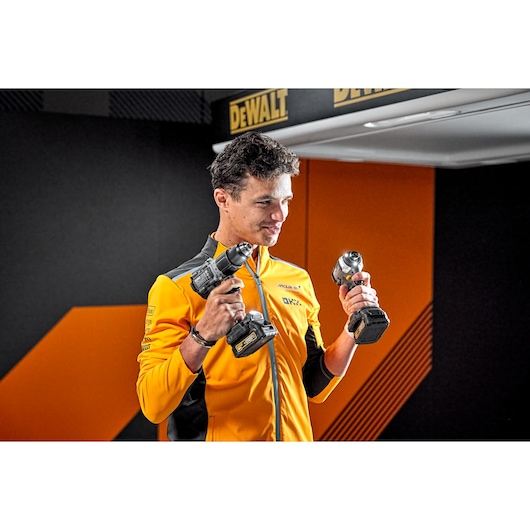 Person in yellow jacket holding two DEWALT power tools, standing in a DEWALT-branded area.