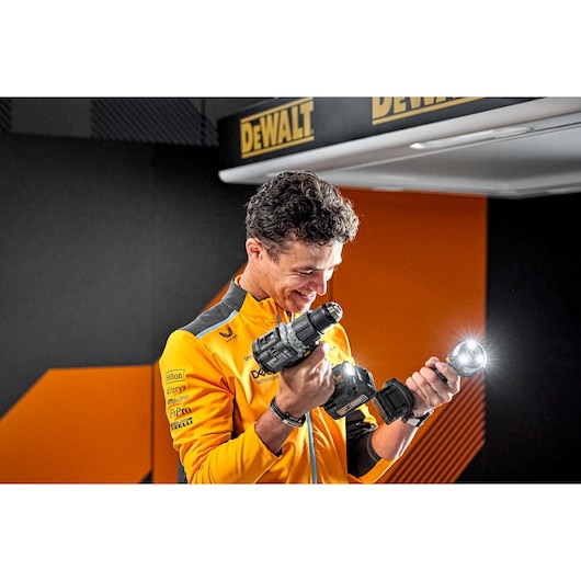 Person in yellow holding DEWALT cordless drill and LED flashlight, brand logo visible in background.