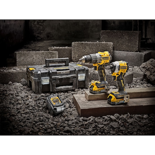 DEWALT tool set with two cordless drills, charger, and case on a rocky construction site.