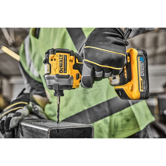 Gloved hand using a DEWALT cordless drill to drill into a metal beam at a worksite.