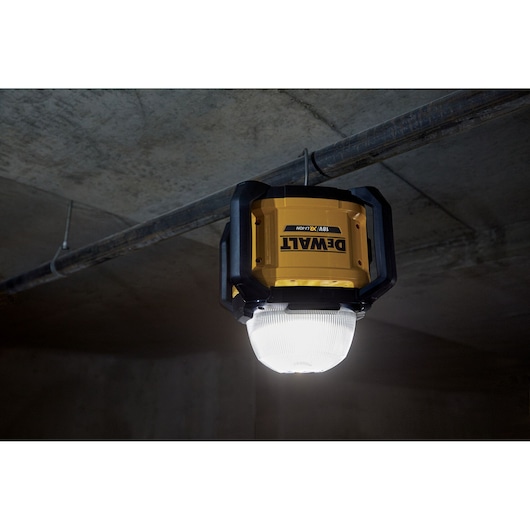 DEWALT DCL074 cordless site light, mounted on a pipe, illuminates a concrete room.