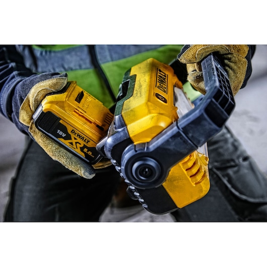 Gloved hands insert a DEWALT 18V battery into a yellow DCL077 work light.
