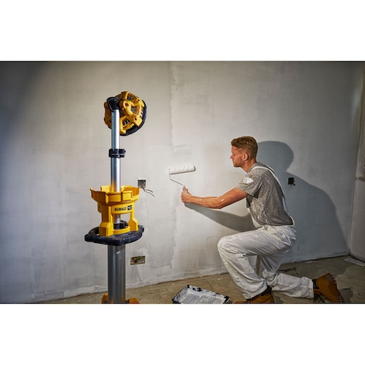 DEWALT DCL079 work light on tripod used by a painter rolling paint on a wall in a room under renovation.