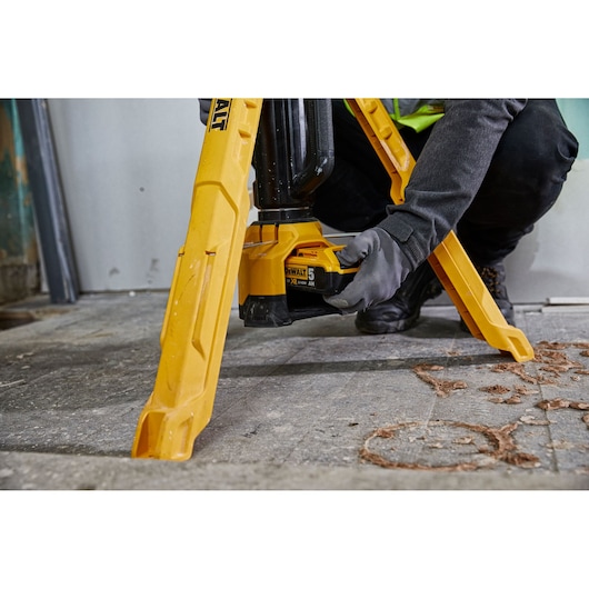 Person installs battery in a yellow DEWALT tripod work light on a workshop floor.