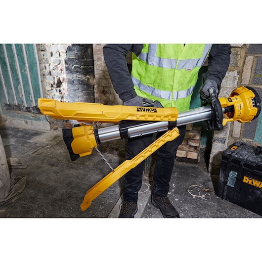 Person sets up a yellow DEWALT tripod work light in an industrial environment with brick walls and equipment.