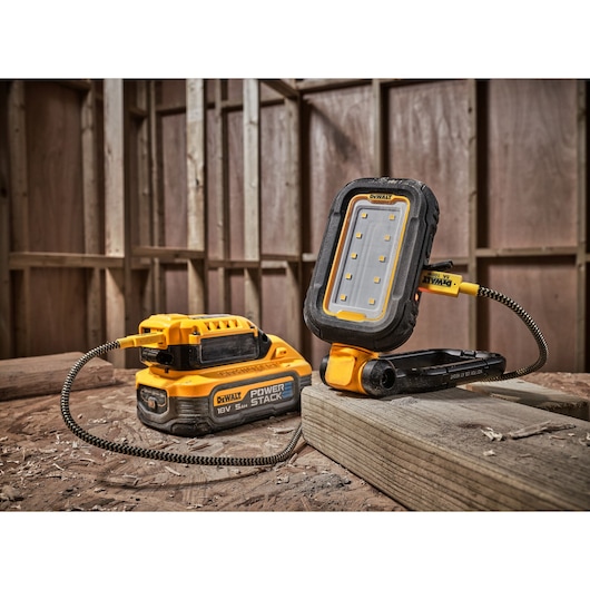 A DEWALT portable LED work light connected to a DEWALT Power Stack 18V battery, placed on a wooden surface inside a