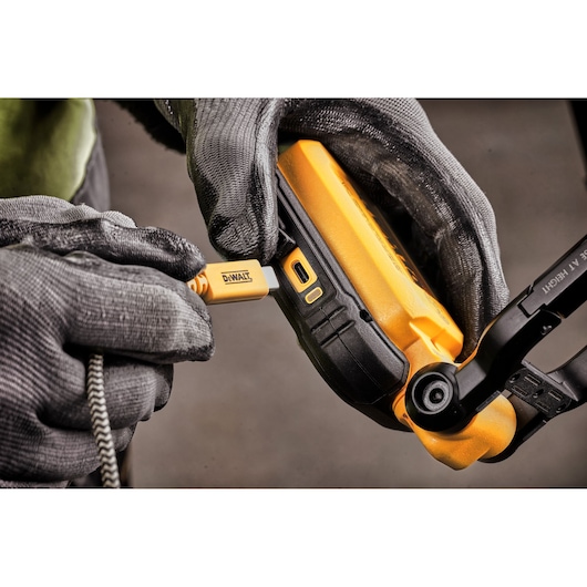 Close-up image of a person wearing gloves plugging a DEWALT charging cable into a DEWALT portable device.