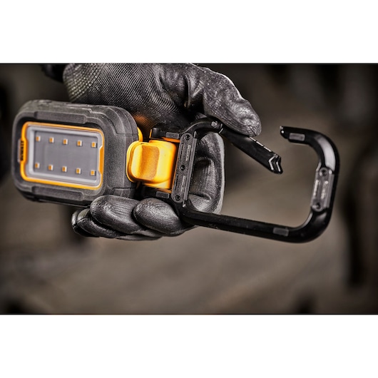 A close-up of a hand wearing a black work glove holding a DEWALT portable LED work light with an integrated black and yellow