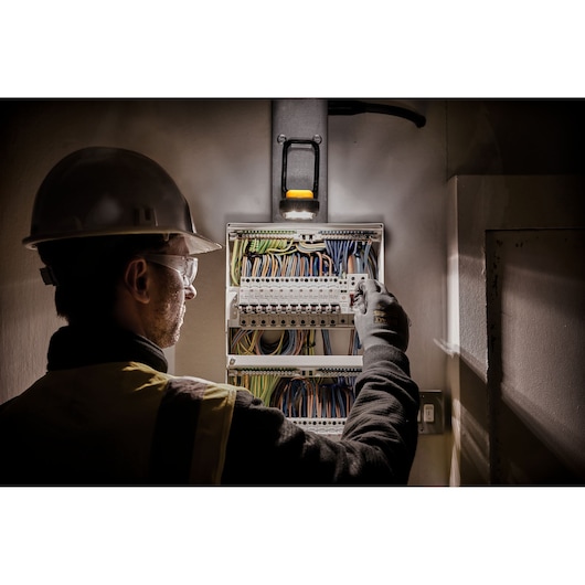 A person wearing safety gear, including a helmet and gloves, is working on an electrical panel with multiple colored wires