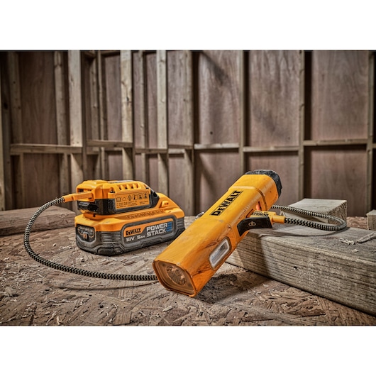 A DEWALT DCL183 portable LED work light connected to a DEWALT 18V POWERSTACK battery, placed on a construction site with