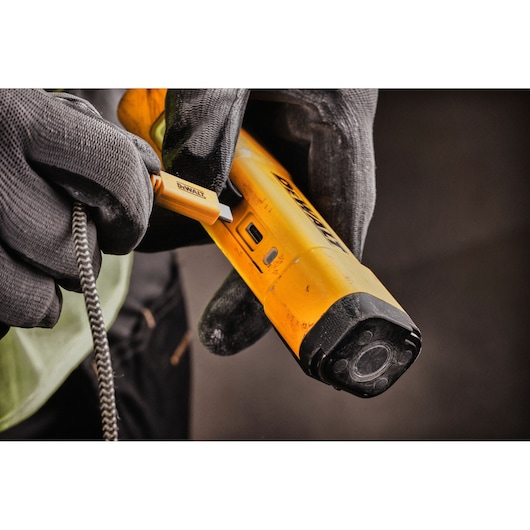 A close-up of gloved hands connecting a charging cable to a yellow DEWALT portable inspection light.
