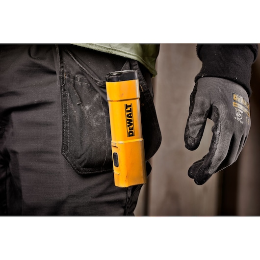 A close-up of a person wearing work gloves and carrying a yellow DEWALT portable light in the pocket of black work trousers.