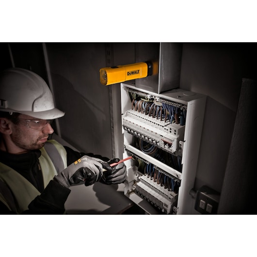 A DEWALT DCL183 LED flashlight is mounted above an open electrical control panel, illuminating the workspace. A person