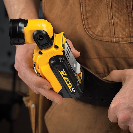 Hand holding a DEWALT DCL510N 12V compact flashlight clipped to a tool belt.