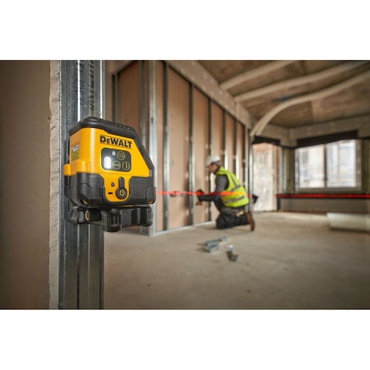DEWALT laser level attached to metal framing. Worker in background aligns materials using red laser line.