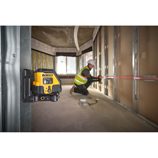 DEWALT laser level mounted in construction, worker aligns metal framework using red laser line.