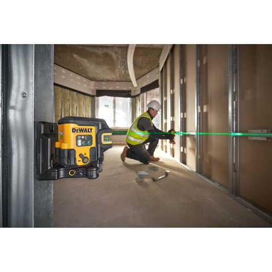DEWALT laser level projecting a green line, used by a worker for aligning framing on a construction site.