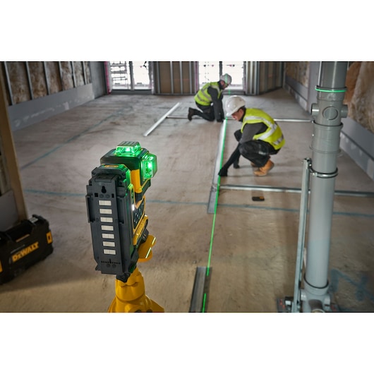DEWALT green laser level used by two workers in safety gear for measuring and alignment on a construction site.