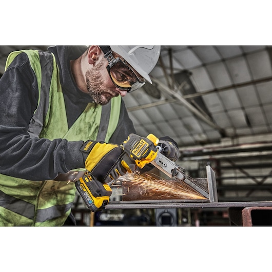 Worker uses DEWALT DCM200E2T tool to grind metal, creating sparks in an industrial workshop setting.