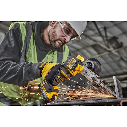 Worker using DEWALT cordless belt file tool on metal, creating sparks in an industrial setting.