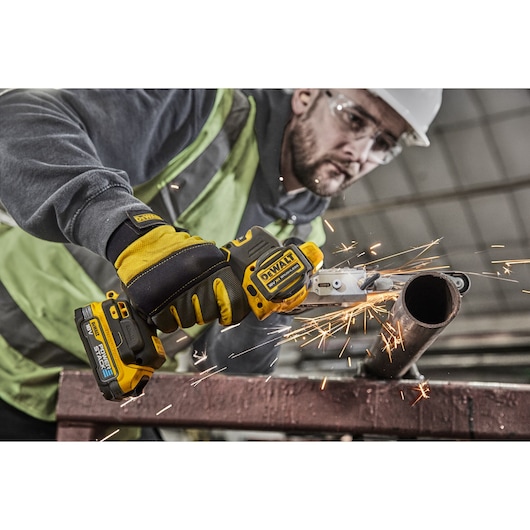 Worker uses DEWALT cordless metal cutter, sparks fly while cutting a steel pipe at work site.
