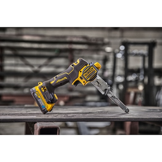 A DEWALT DCM200E2T cordless electric chainsaw with yellow and black design is placed on a metal surface in an industrial workshop setting.