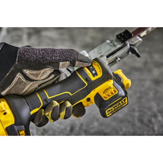Gloved hand adjusting settings on a DEWALT cordless power tool, close-up view of the handle and controls.