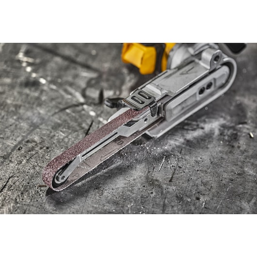 Close-up of a DEWALT electric belt file tool on a scratched metal surface, showing sanding belt and tool details.