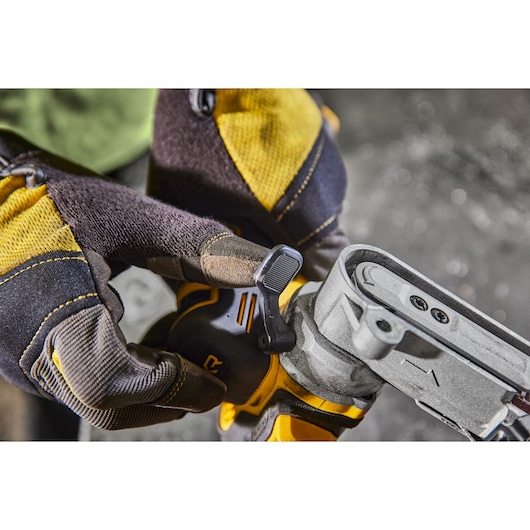 Gloved hand adjusts a DEWALT tool lever on a metallic device, yellow and black gloves visible, close-up view.