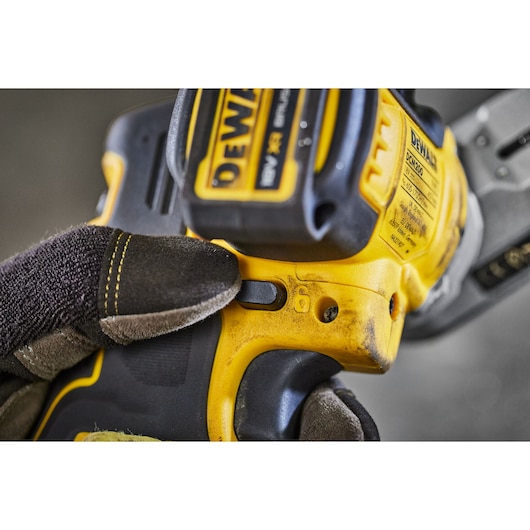 Gloved hand pressing button on yellow DEWALT power tool with visible model label.