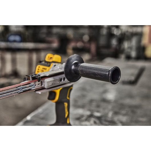 Close-up of a DEWALT cordless belt sander with a handle, shown on a workbench in an industrial setting.