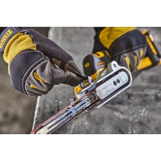 Gloved hands adjust a DEWALT DCM200NT power tool, focusing on the sanding belt mechanism.