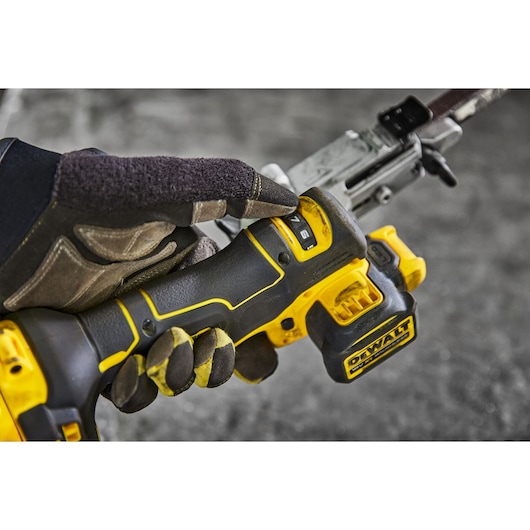 Gloved hand adjusting speed on a yellow DEWALT cordless tool during use on a metal surface.