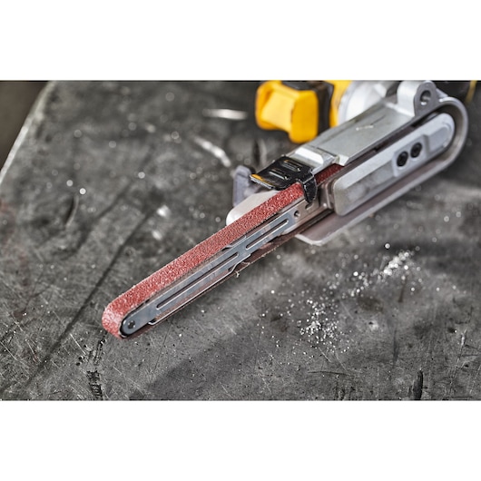 Close-up of a DEWALT belt sander on a metal surface. The sanding belt is visible and red.