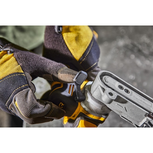 Gloved hands adjusting a lever on a DEWALT power tool, focusing on details and textured grip.