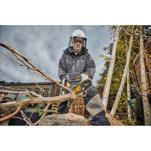 Person using a DEWALT chainsaw outdoors, cutting a tree branch while wearing protective gear.