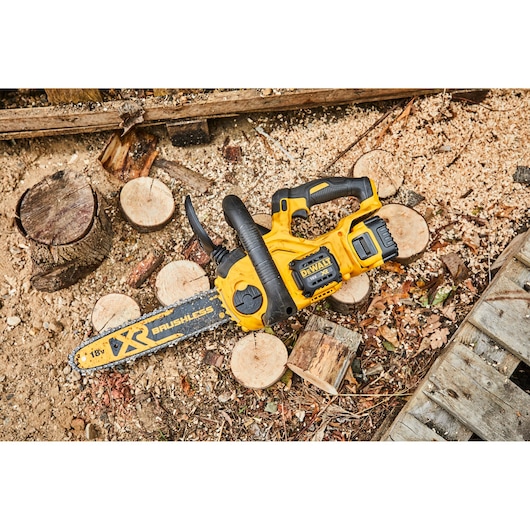 DEWALT cordless chainsaw lies on cut logs and sawdust outdoors, ready for use in wood cutting tasks.