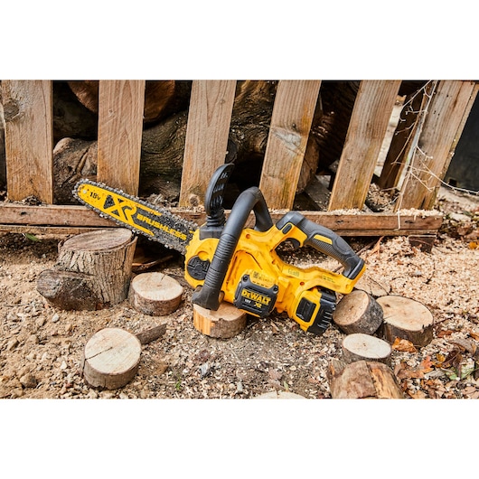 Yellow DEWALT cordless chainsaw on the ground with cut wood pieces and sawdust outdoors.