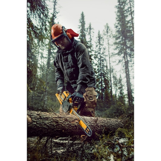 Person using a DEWALT chainsaw to cut a log in a forest, wearing safety gear and gloves.