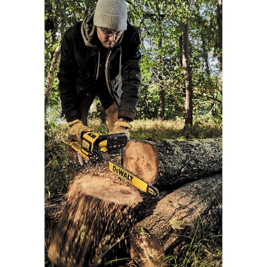 Person uses a DEWALT chainsaw to cut a log outdoors in a forested area.