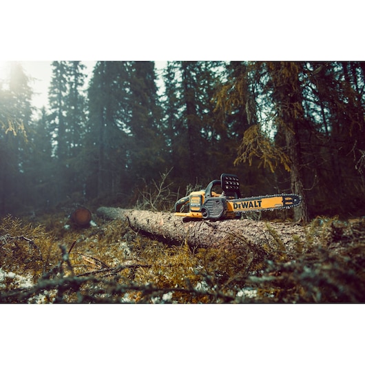 DEWALT chainsaw placed on a fallen tree in a forest, surrounded by foliage and pine trees.