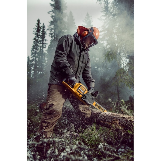 Person using a DEWALT chainsaw outdoors to cut a log, wearing safety gear in a misty forest environment.