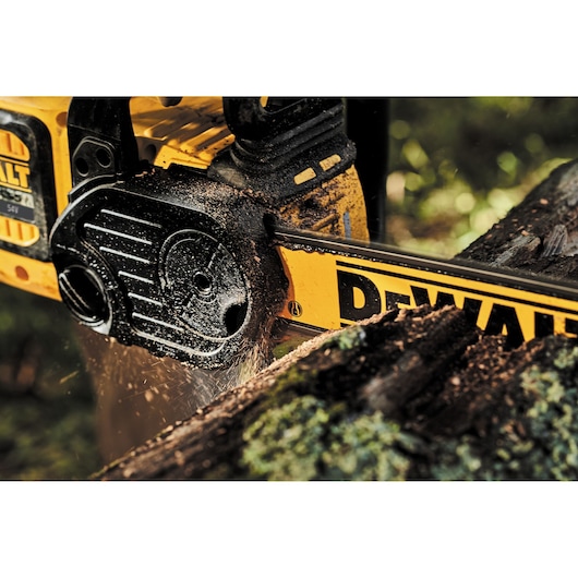 Close-up view of a yellow DEWALT chainsaw cutting through a log, with wood debris and sawdust flying as the tool operates outdoors.