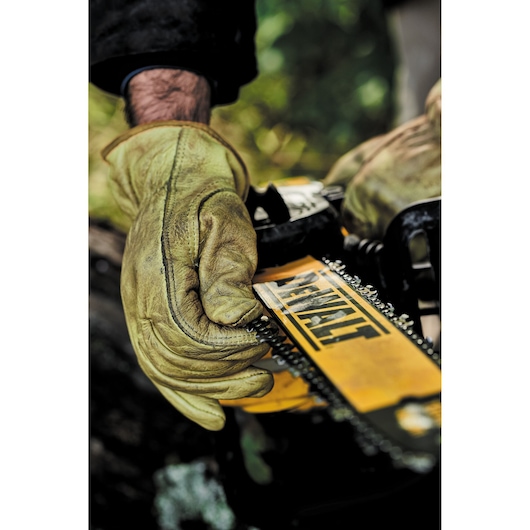 Close-up of gloved hands adjusting the chain on a yellow DEWALT chainsaw outdoors.