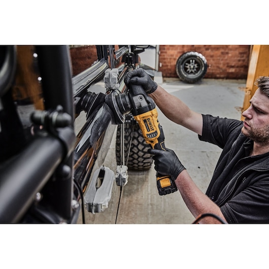 A person wearing black gloves uses a DEWALT cordless polisher to polish the side of a black vehicle in a garage setting.