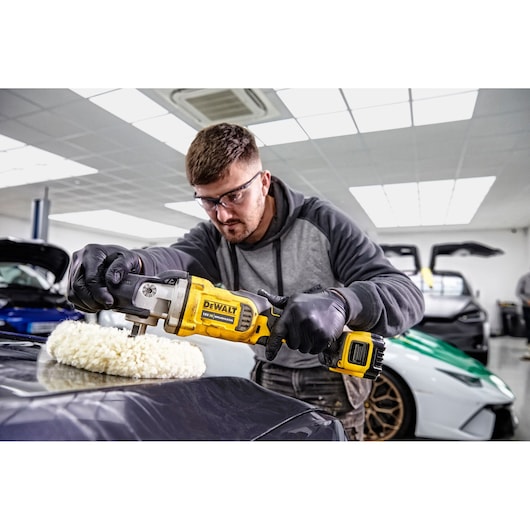 Person uses a DEWALT DCM849P2 cordless polisher to buff a car's hood in a garage.